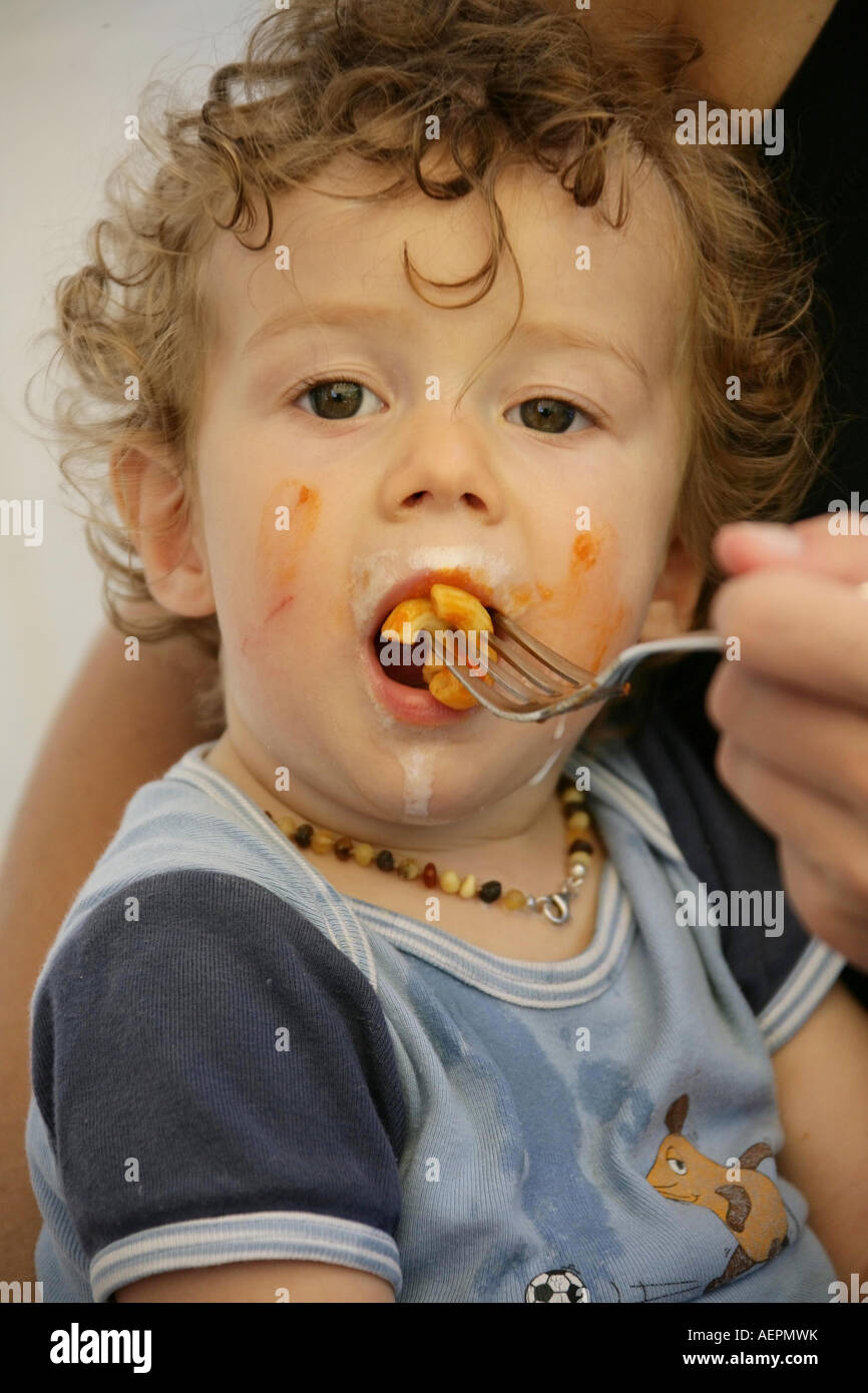 Kleinkind 18 Monate alt JONI mit Bernsteinkette um den Hals beim Essen mit verschmiertem Gesicht Model Released Stock Photo