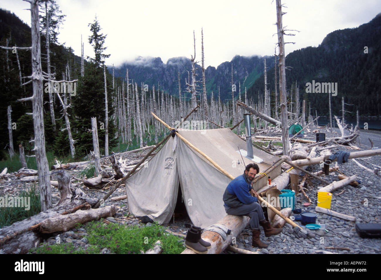 Paul Splan outside wall tent with dead trees on a gravel beach Kenai