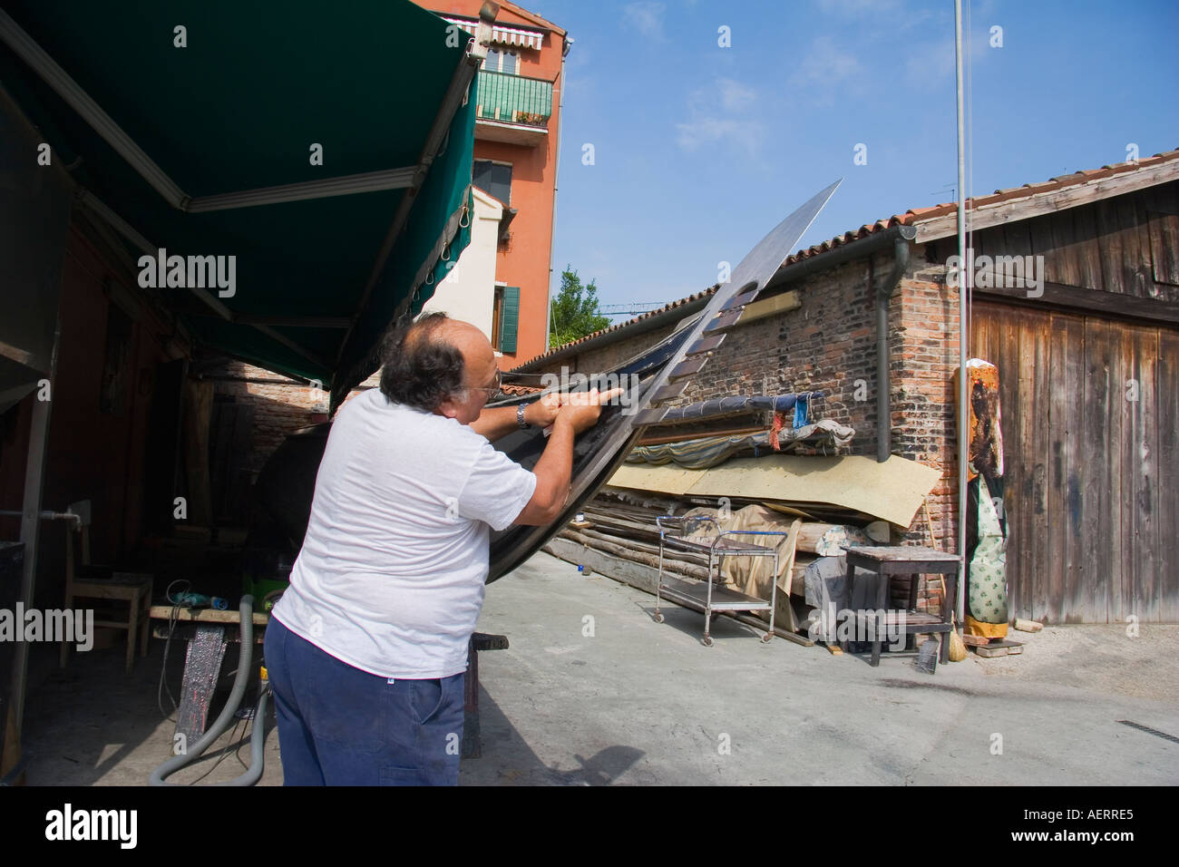 Craftsman using chisel to scrap paint on gondola in the boatyard of D Tramontin Figli Venice Italy Stock Photo