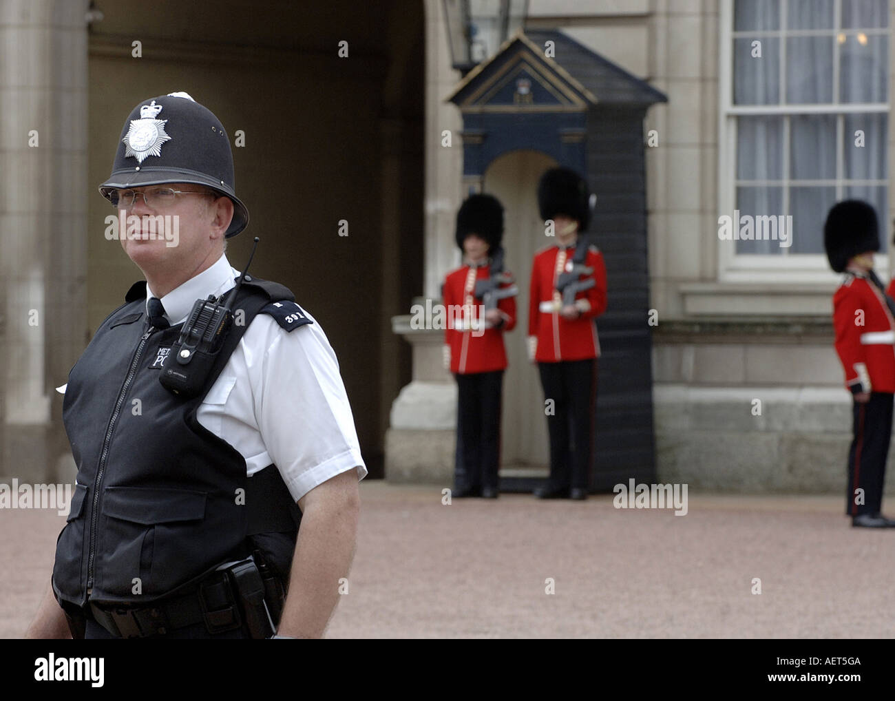 Policeman and Buckingham Palace Guards stand outside Buckingham Stock