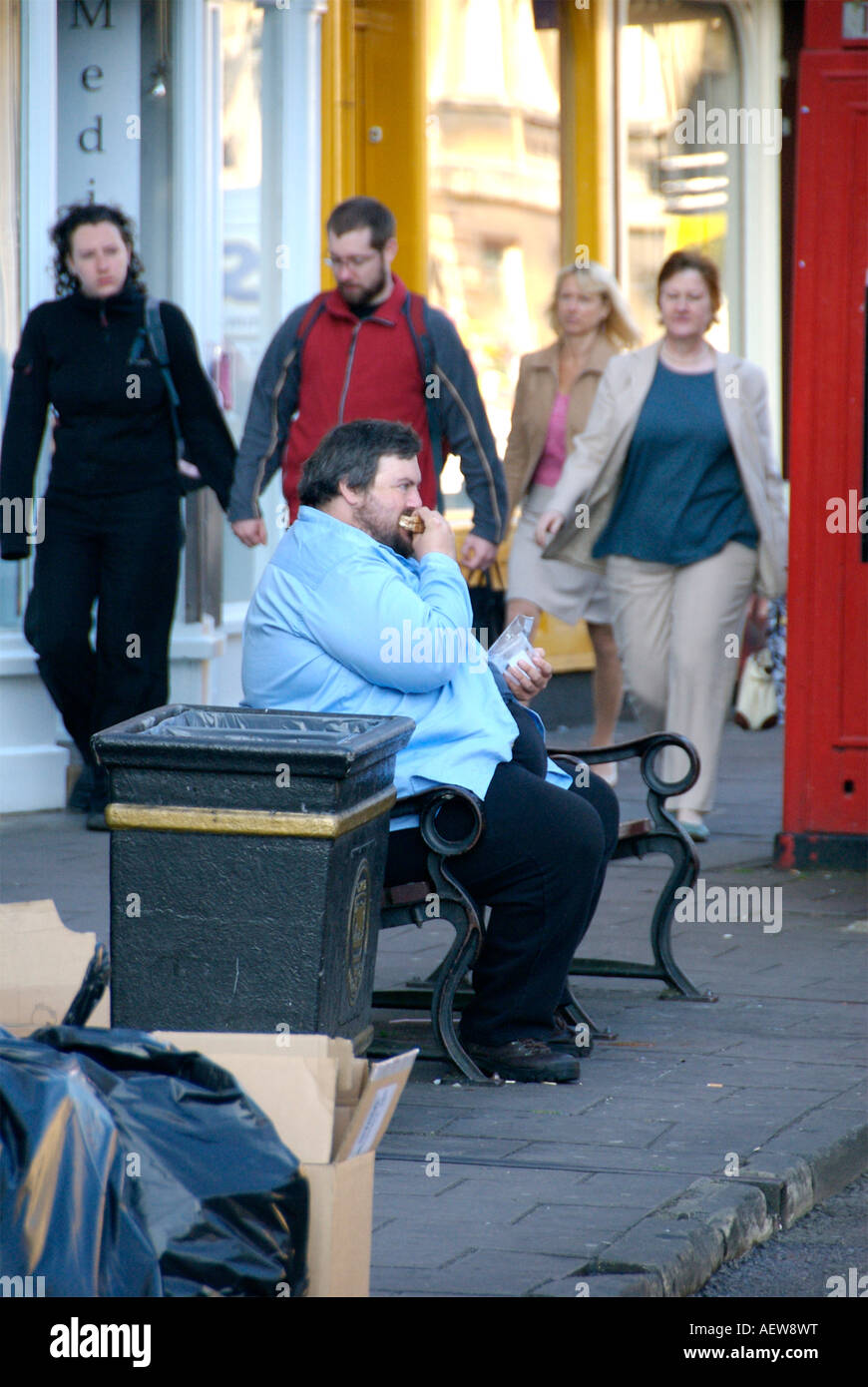 A big fat obese man  sat down eating food outside in the high street in Oxford Stock Photo