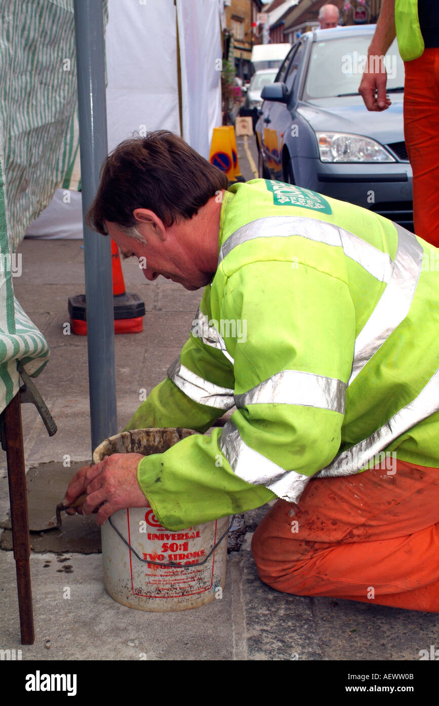 Adult male wearing hi-visibility clothing cementing in a street sign post Stock Photo