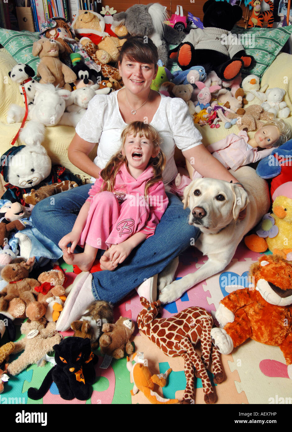 Smiling mother and laughing five year old blonde daughter with soft toys and pet dog Stock Photo