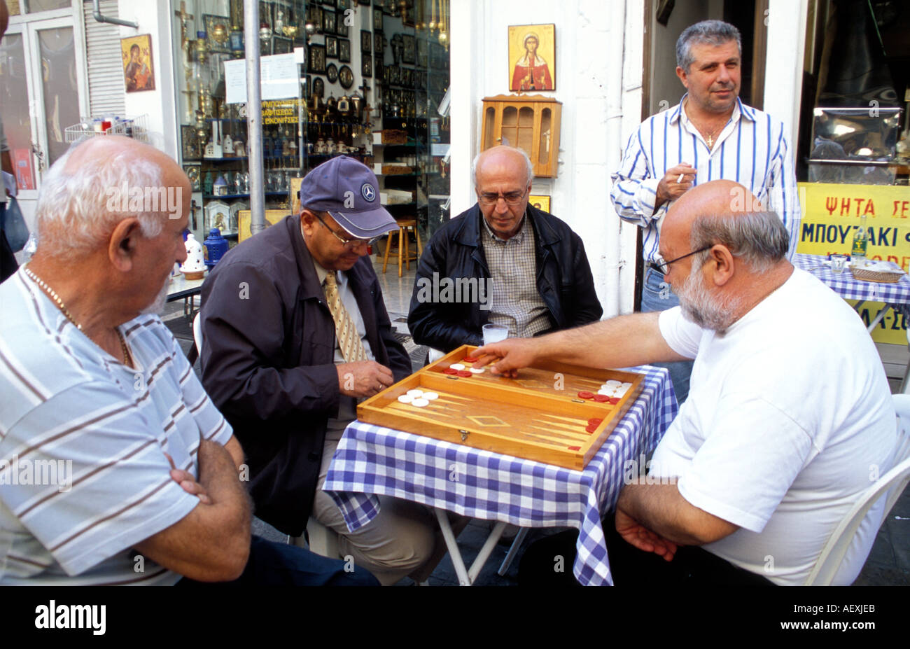 Typical Greek Street Scene. A bunch of men gathered around a table watching a game of backgammon / Tavli Stock Photo
