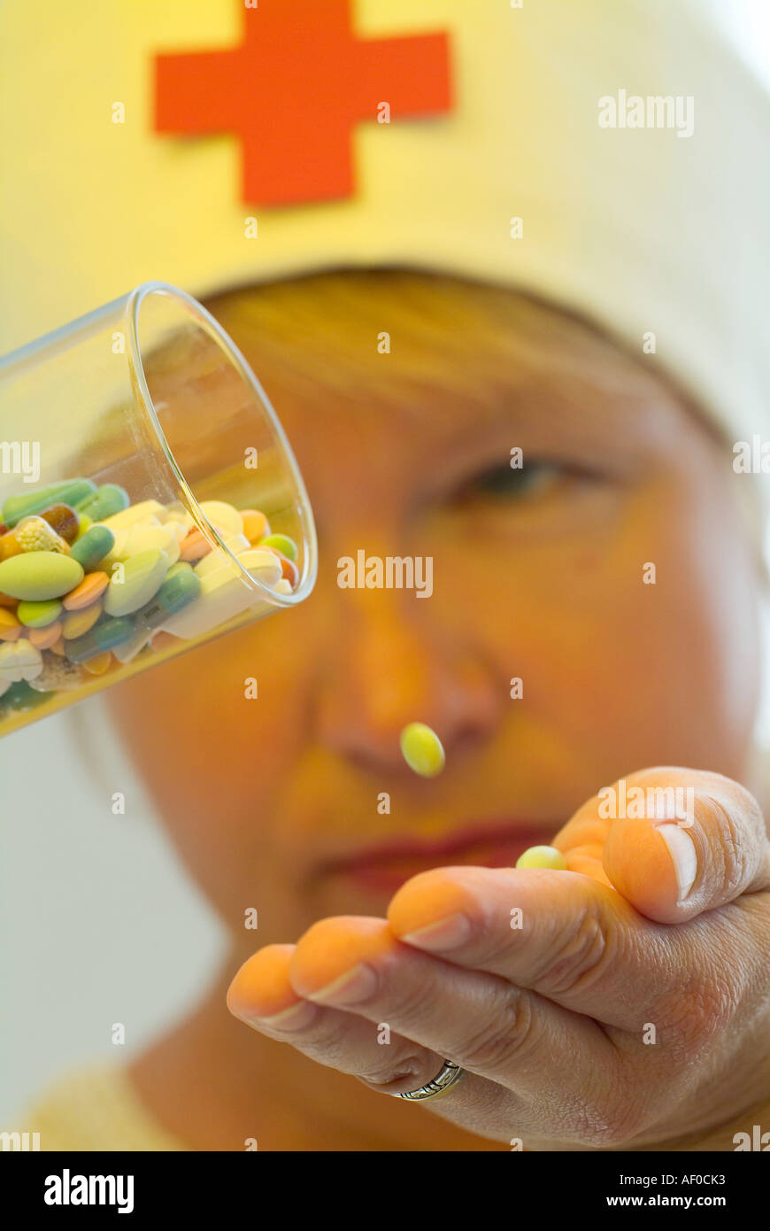 one pill falling out from a glass filled with pills in different colours and forms down on an open hand in background a nurse Stock Photo