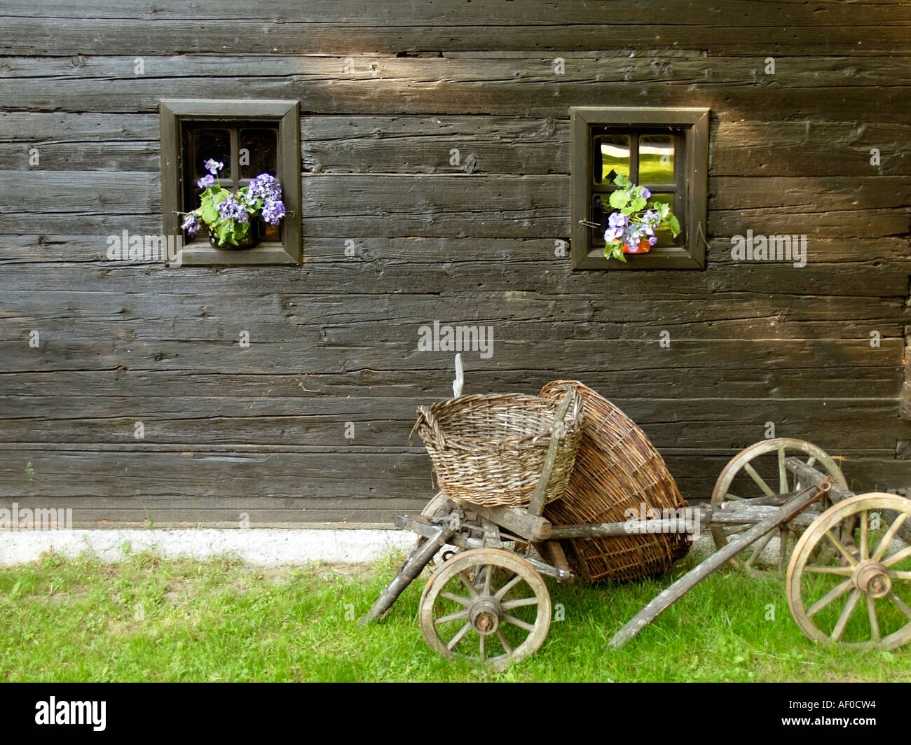 old blockhouse log house with an old cart barrow in the flower park Mozirski Gaj Stock Photo