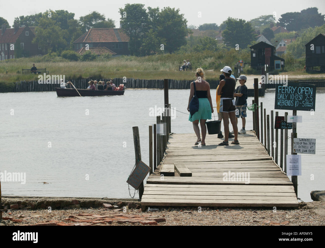 People wait on river jetty for passage in a rowing boat, The Walberswick to Southwold Ferry. Stock Photo