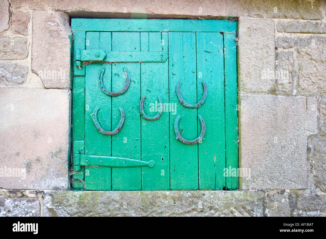 Painted Wooden Hay Loft Door Set in a Stone Wall with Five Horseshoes Attached Stock Photo