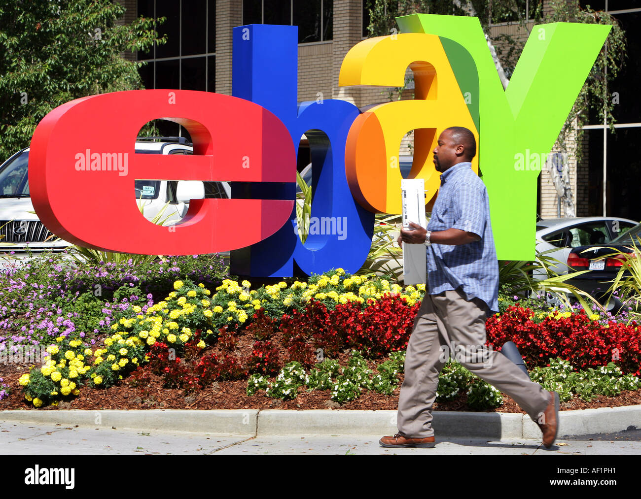 ebay headquarters in San Jose California. An employee carries a computer in front of the ebay logo Stock Photo