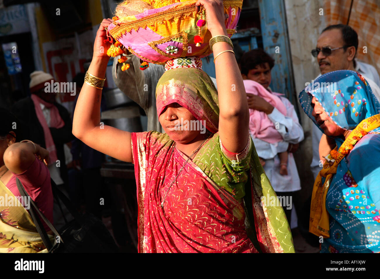 Indian female carrying basket of garlands on head walking through crowd celebrating holi spring festival of colours, Dwarka, Gujarat, India Stock Photo