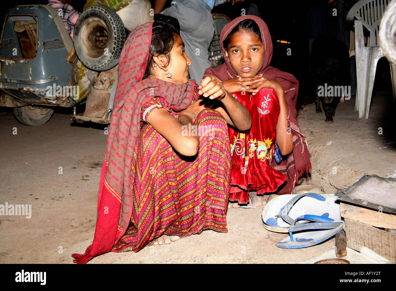 Two young Indian girls crouching on ground in High Street, Dwarka ...