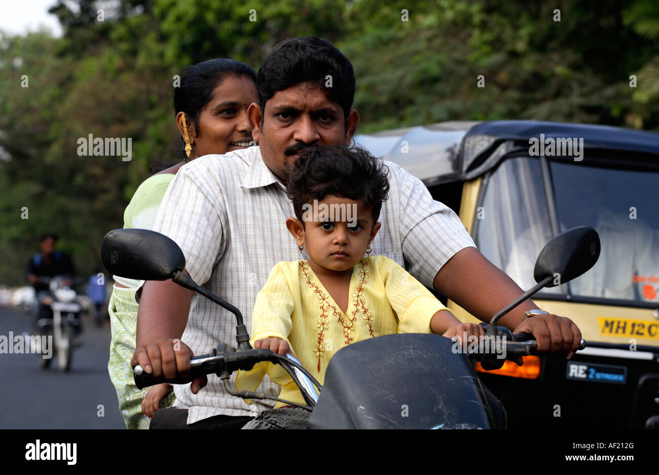 Indian family of three riding on motorbike in busy traffic without crash helmets, Pune, India Stock Photo