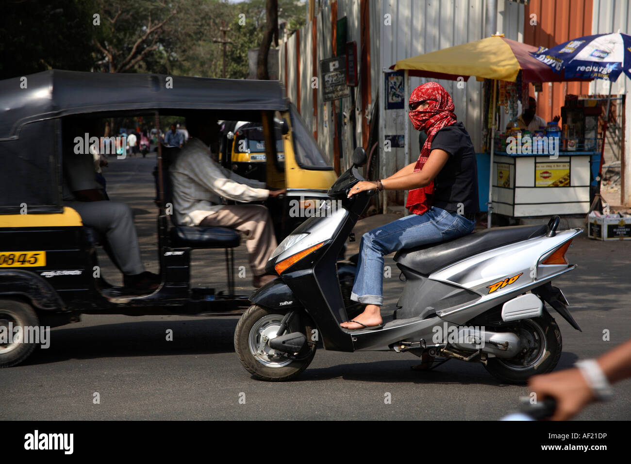 Indian female with head covered driving scooter without helmet in traffic in Pune, India Stock