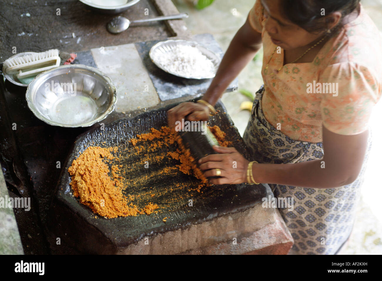 Goan Indian woman grinding coconut and chillies for curry with flat