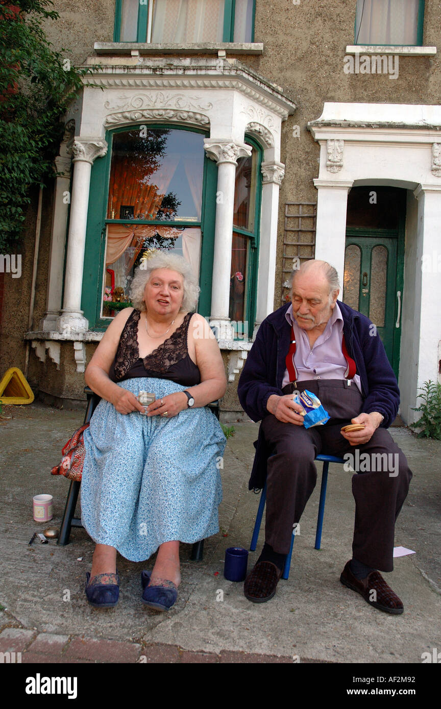 Proud and characterful older couple sitting on pavement outside their home. Stock Photo