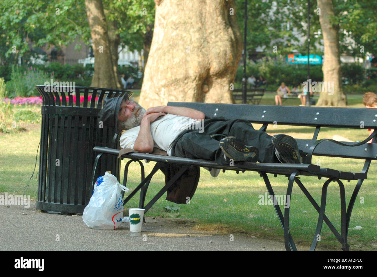 Homeless man sleeping on a park bench in Russell Square London Stock