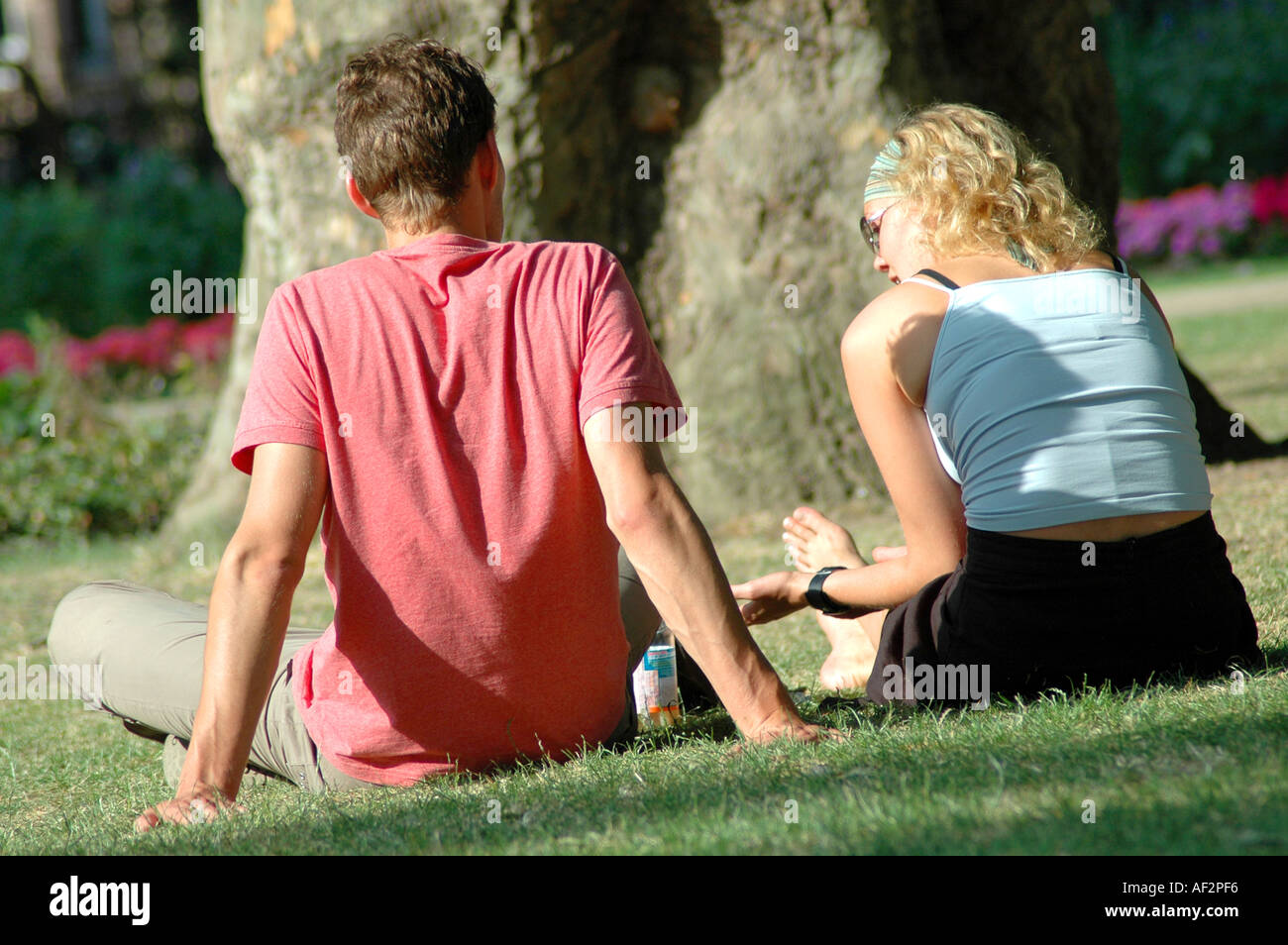 Tourist couple sitting on the grass in a Central London park in summer Stock Photo