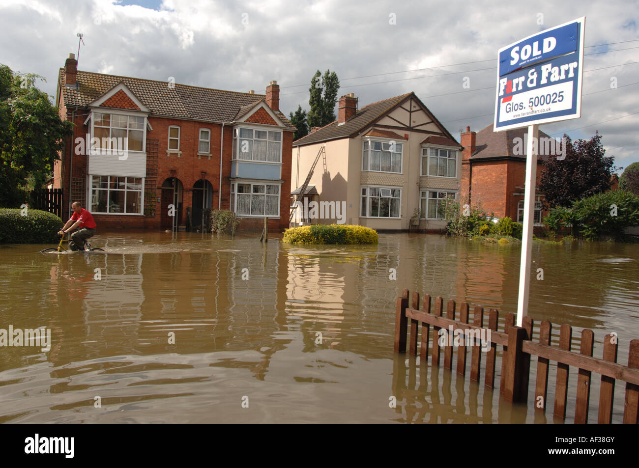 Cyclist passes Sold house sign in a flooded  Road in Longford area of Gloucester England July 2007 Stock Photo