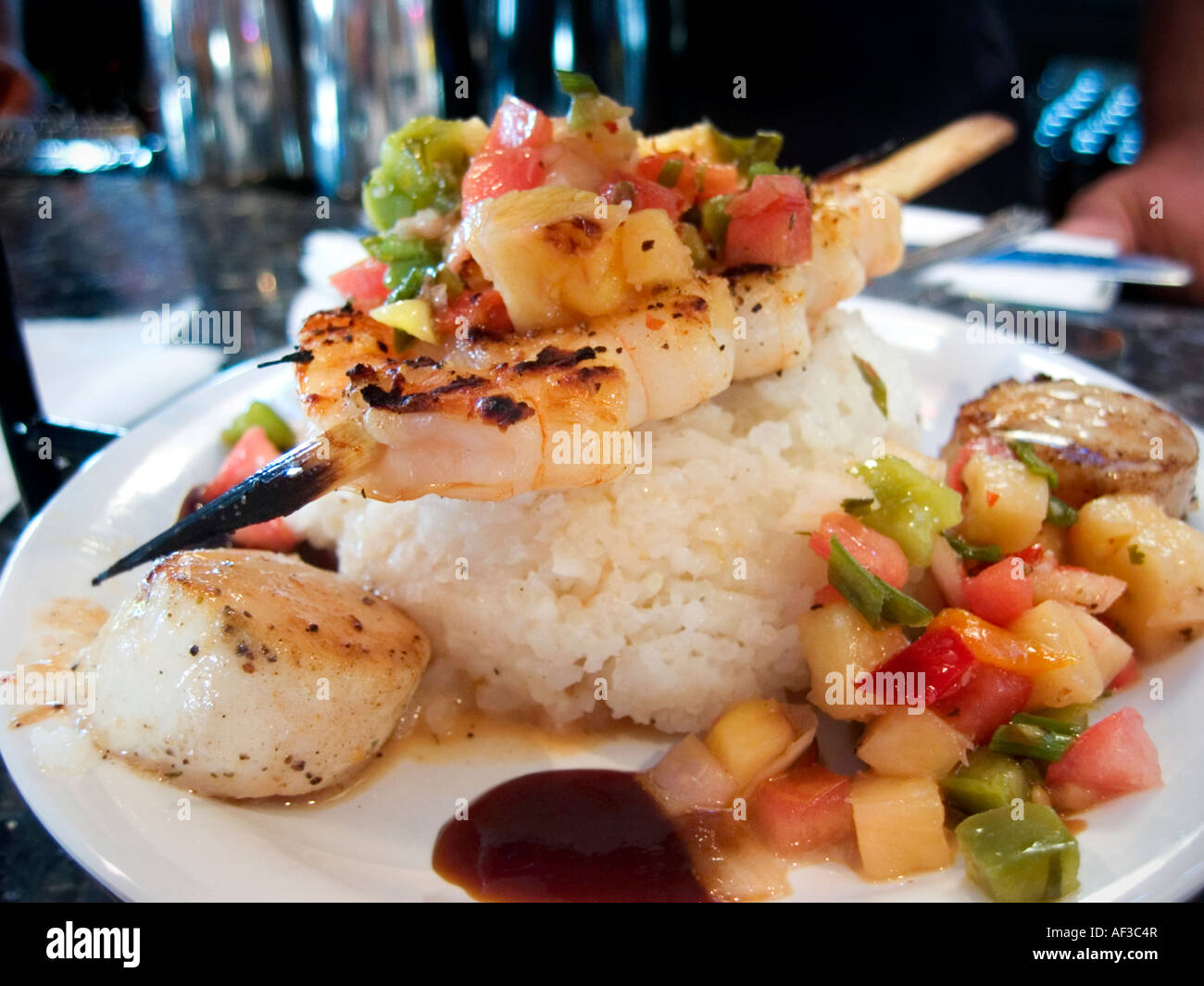 Gourmet presentation of a skewer of grilled shrimp with scallops, rice and chutney. Stock Photo