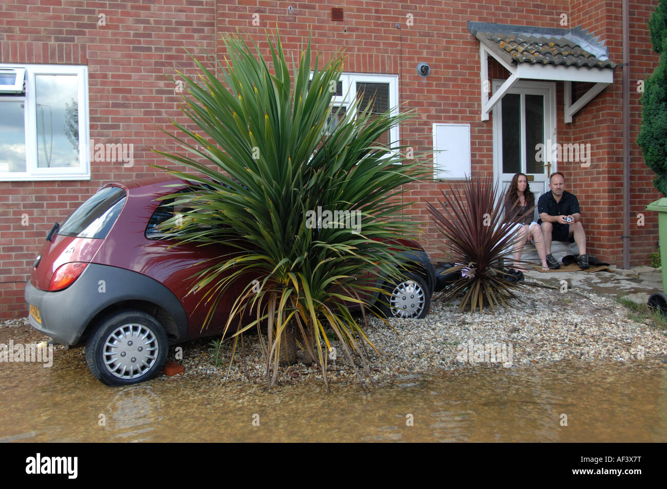 A couple sit at the door of their home and watch the floods next to their car in  Longford area of Gloucester England July 2007 Stock Photo