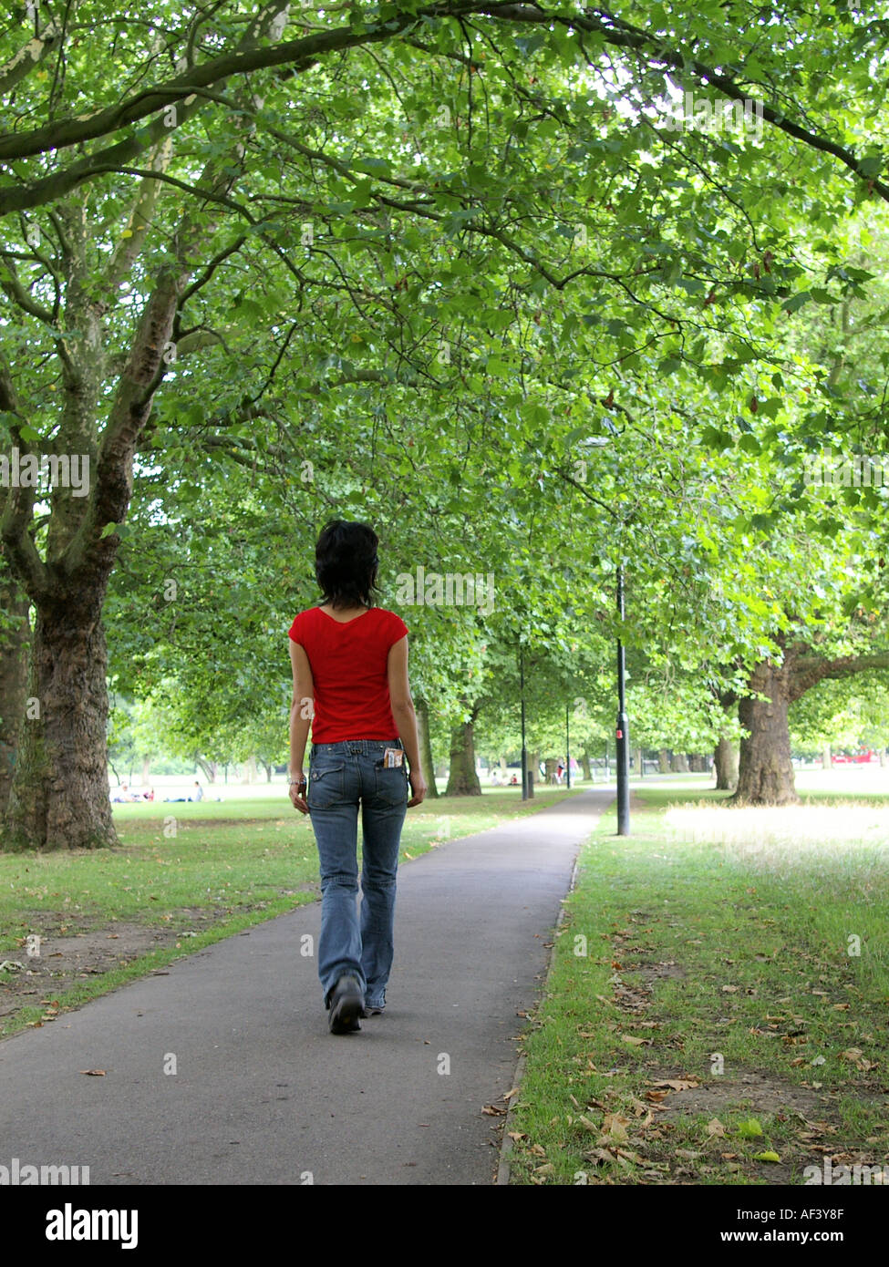 dark haired woman walking alone in park in jeans in Clapham London with visible tobacco pouch in back pocket. Stock Photo