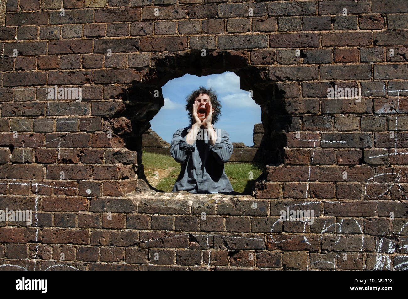 Composer and director of The Shout choir Orlando Gough shouting through a hole in a wall. Stock Photo
