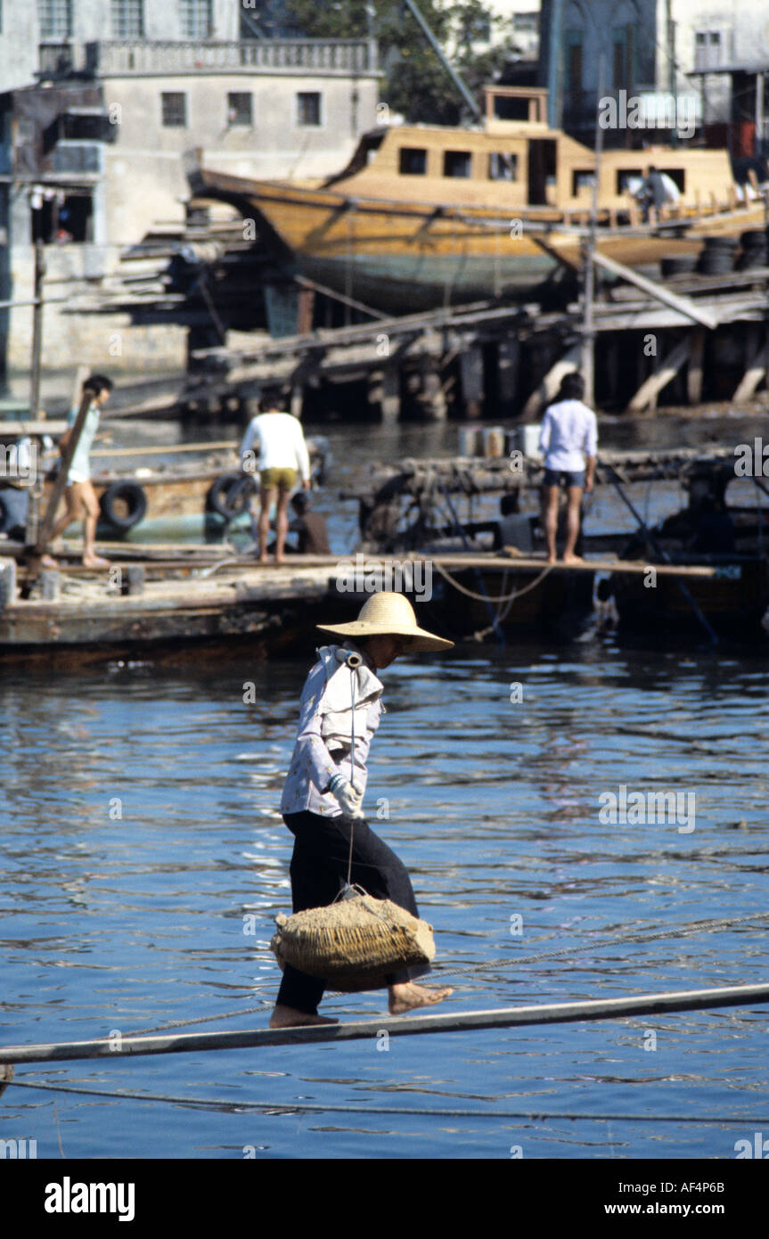 Local worker carries heavy load from a junk via narrow plank over water using traditional yoke on Peng Chau Island Hong Kong Stock Photo