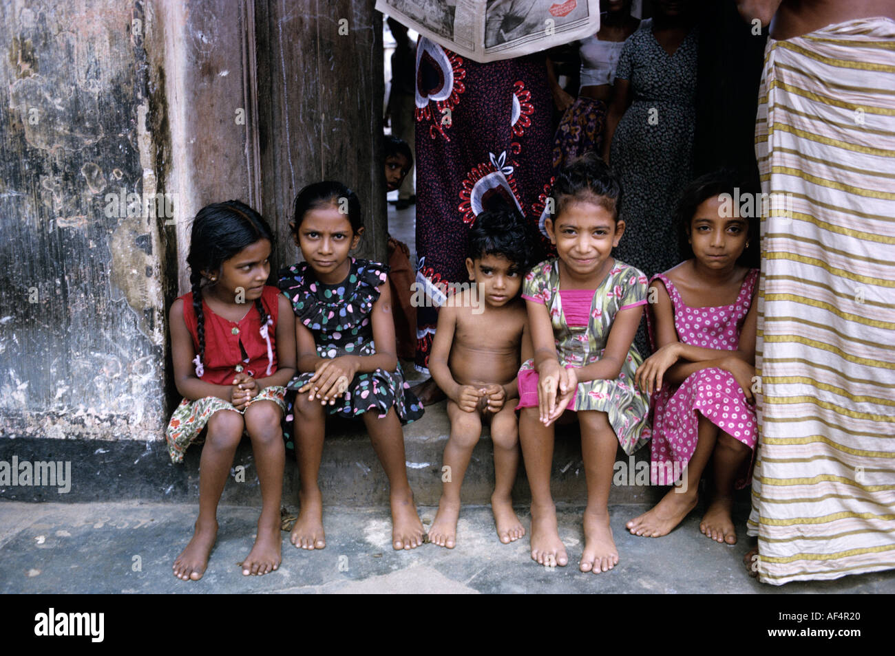 Group of five local children sitting shyly in a street doorway in Colombo Sri Lanka Stock Photo