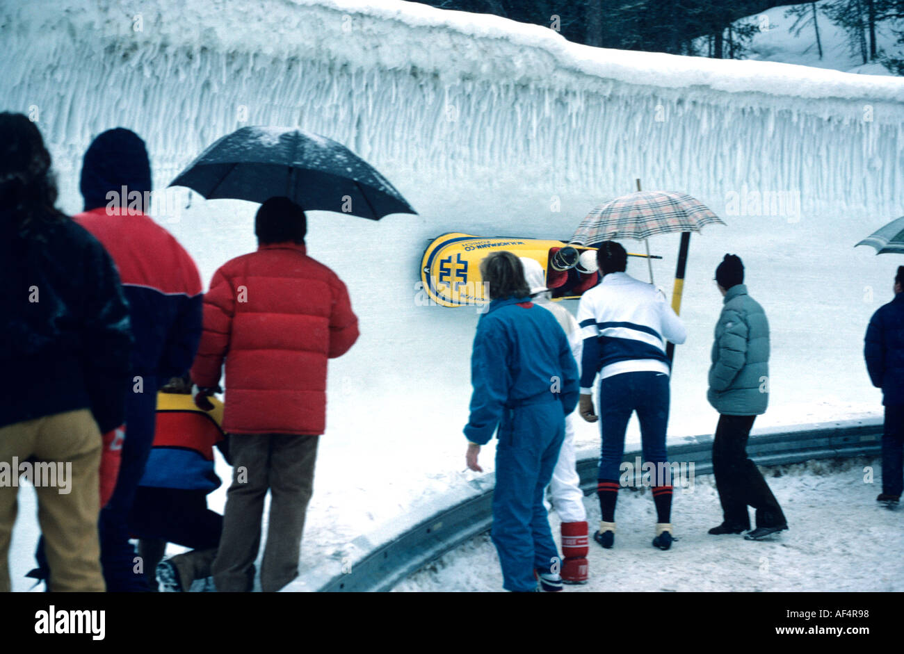 People watch two man toboggan bank hard round a vertical curve on the Cresta Run at St Moritz The Engadin Switzerland Stock Photo