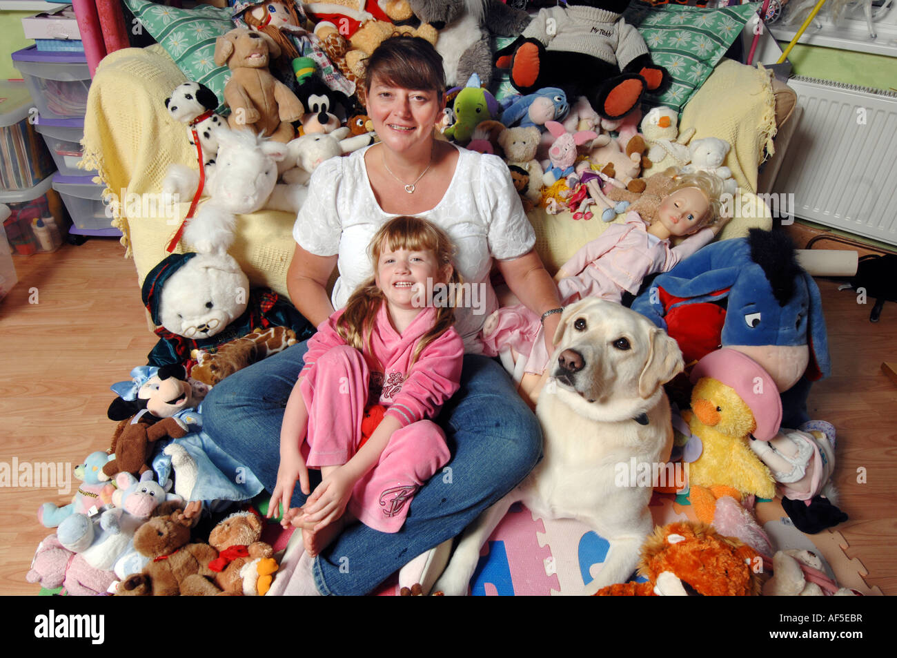 Smiling mum and five year old blonde daughter with soft toys and pet dog Stock Photo