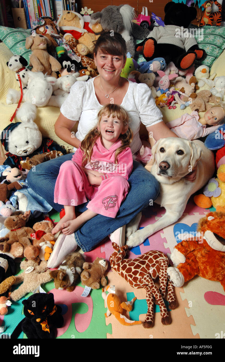 Smiling brunette mother and happy five year old blonde daughter with soft toys and pet dog Stock Photo