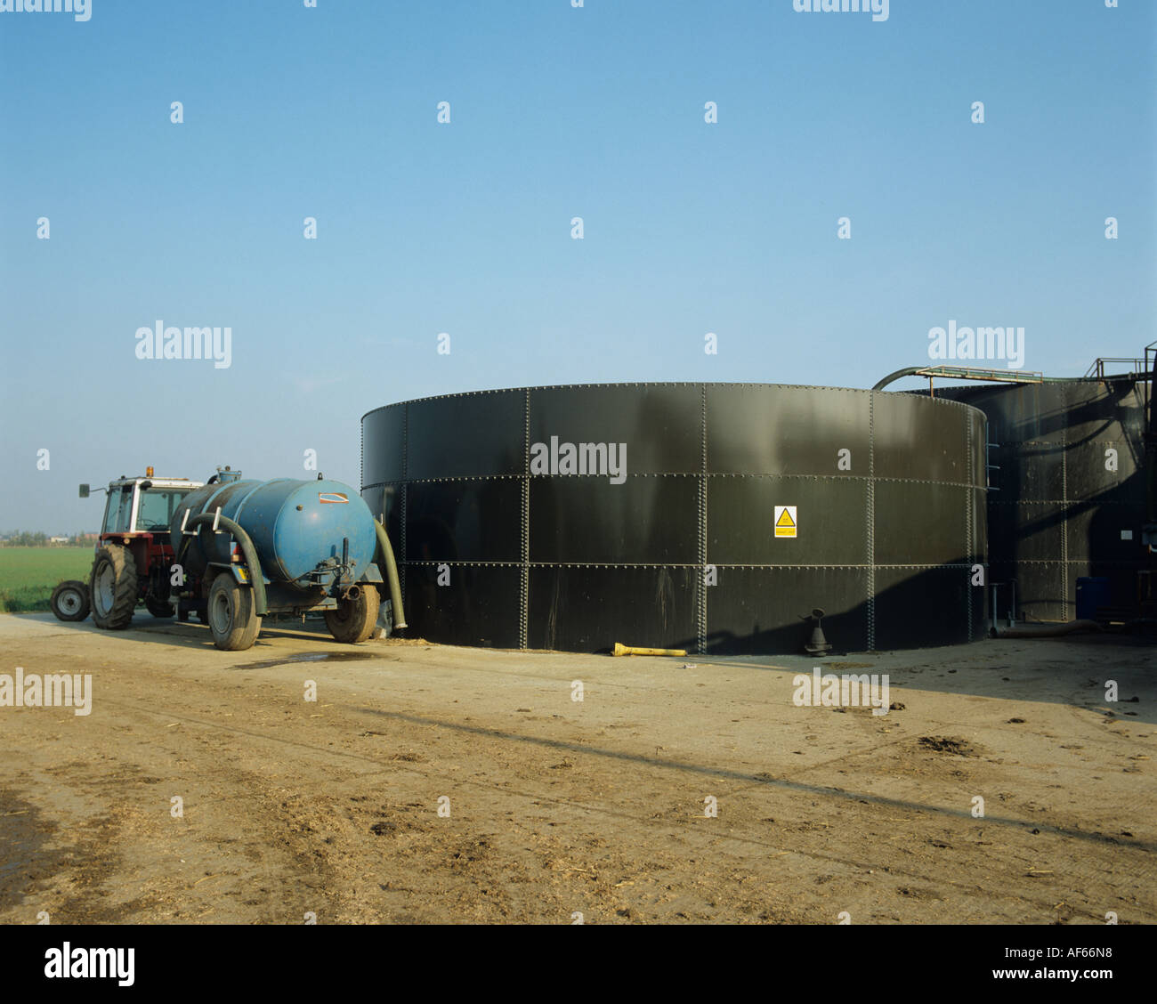 Tractor with slurry trailer alongside large slurry tank Stock Photo