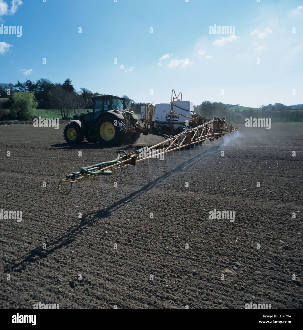 John Deere tractor & trailed sprayer spraying very young spring field bean crop Stock Photo