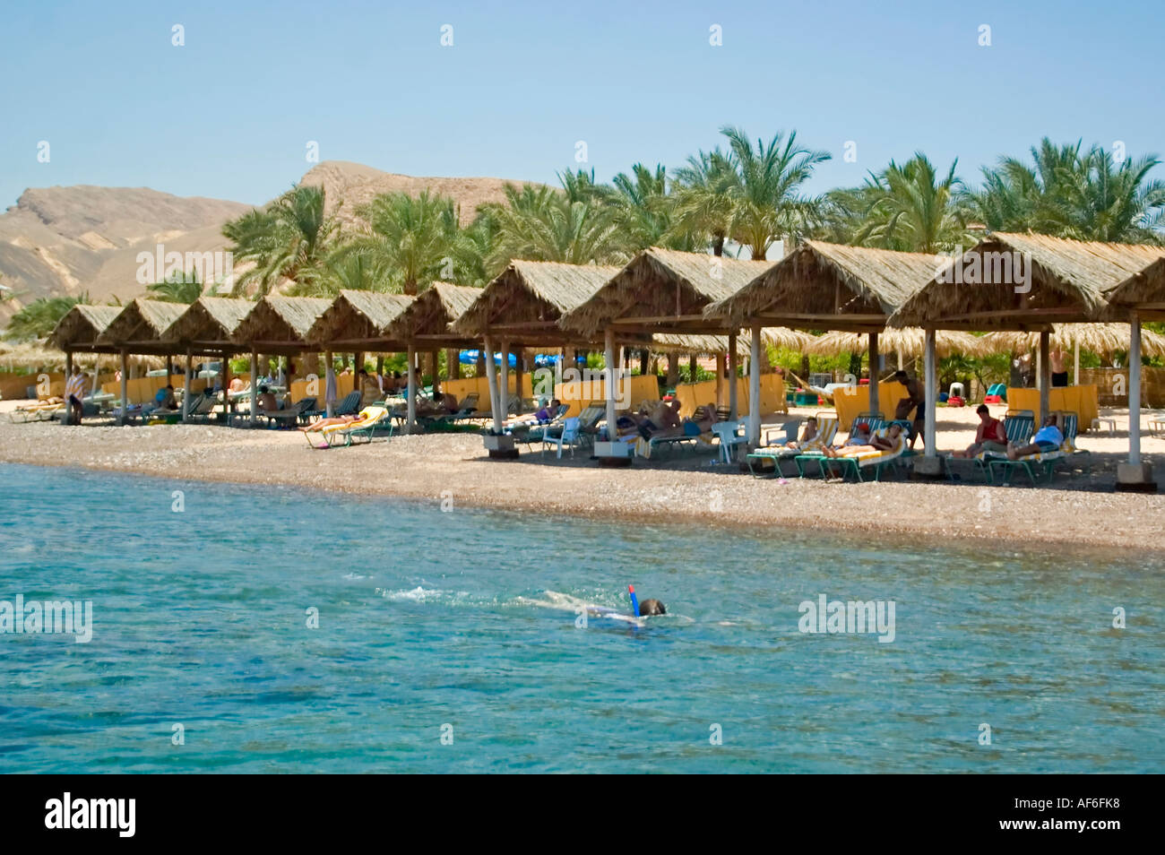 Horizontal wide angle landscape of the coastline at Taba with people sunbathing on the beach, taken from out at sea. Stock Photo