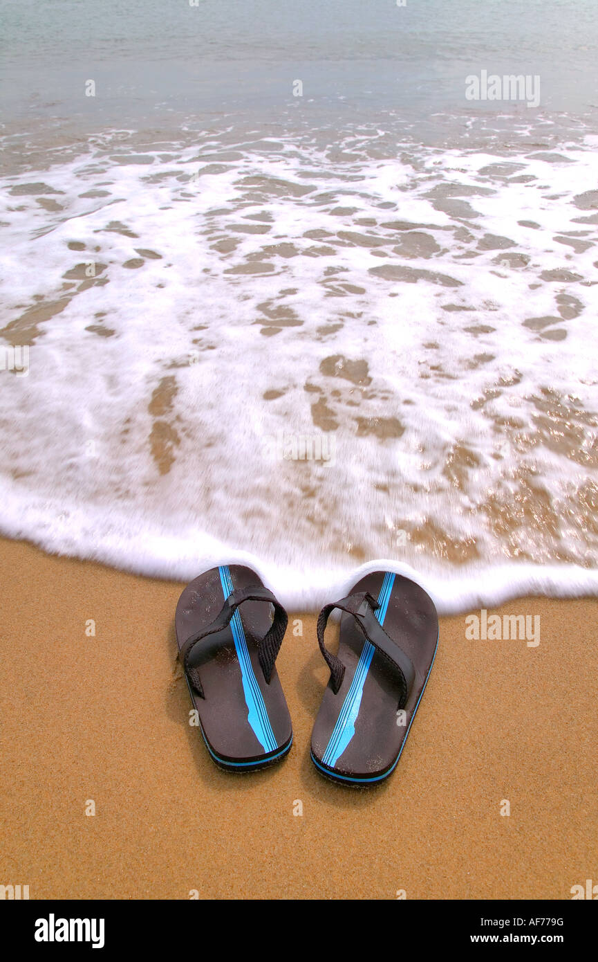 Pair of flip flops at the beach about to be washed away by the tide Stock Photo