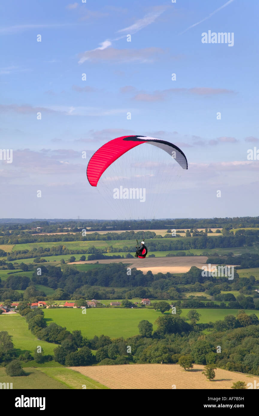 Paraglider with a red and white chute flying across a rural landscape from Butser Hill Hampshire Stock Photo