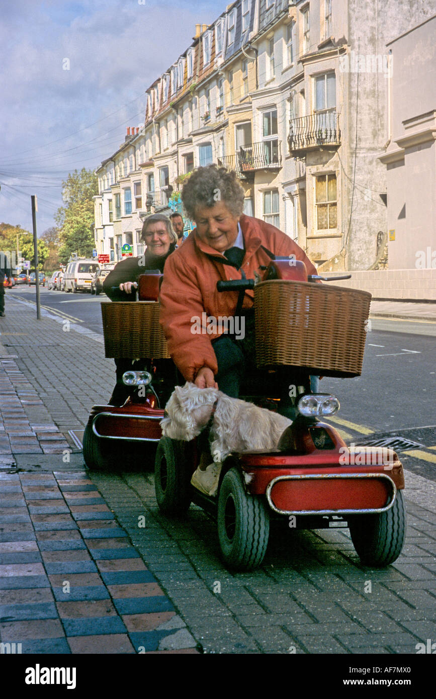 elderly women using electronic scooters for mobility in town with a dog on board Stock Photo
