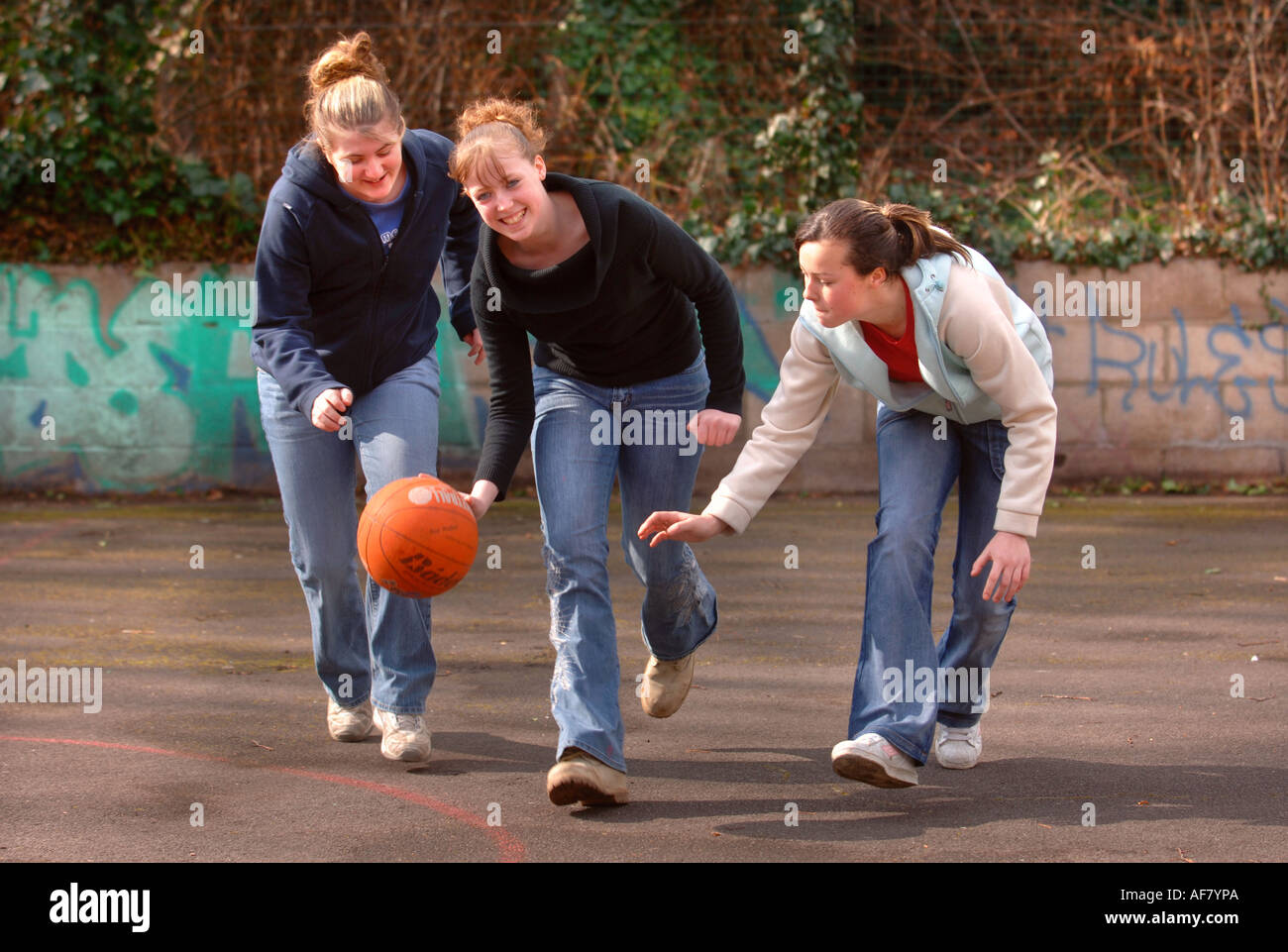 THREE TEENAGE GIRLS PLAYING BASKETBALL AT A YOUTH CLUB UK Stock Photo