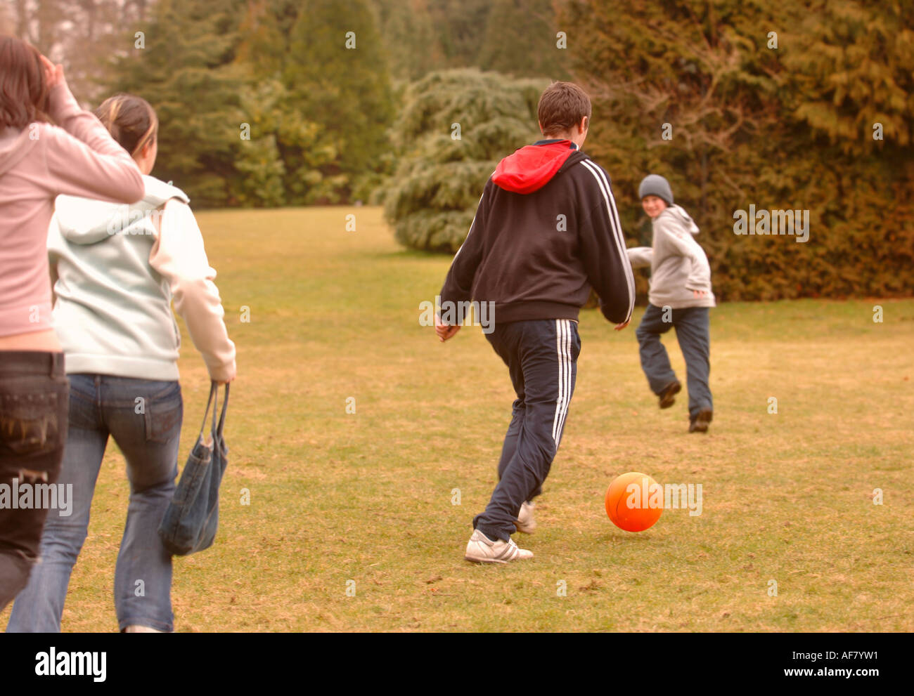 A GROUP OF TEENAGE BOYS AND GIRLS PLAYING FOOTBALL IN A PARK UK Stock Photo
