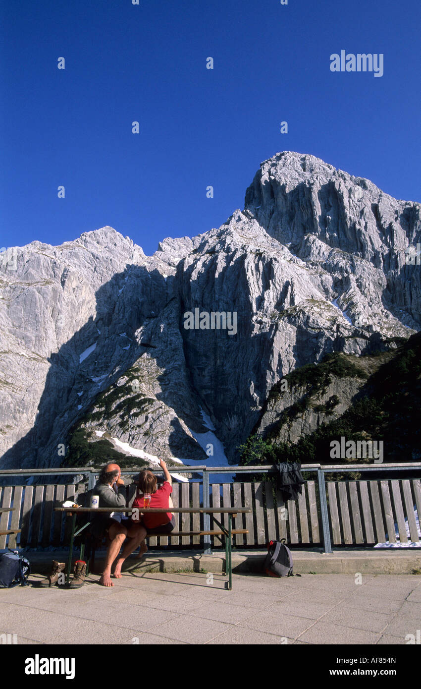 terrace at hut of Stripsenjoch with two hikers looking at Totenkirchl, Stripsenjochhaus, Wilder Kaiser, Tyrol, Austria Stock Photo
