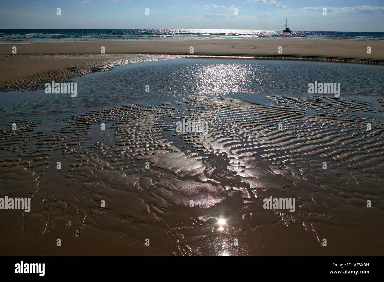Beach scene with sand ripples and a yacht moored out at sea in the distance Stock Photo