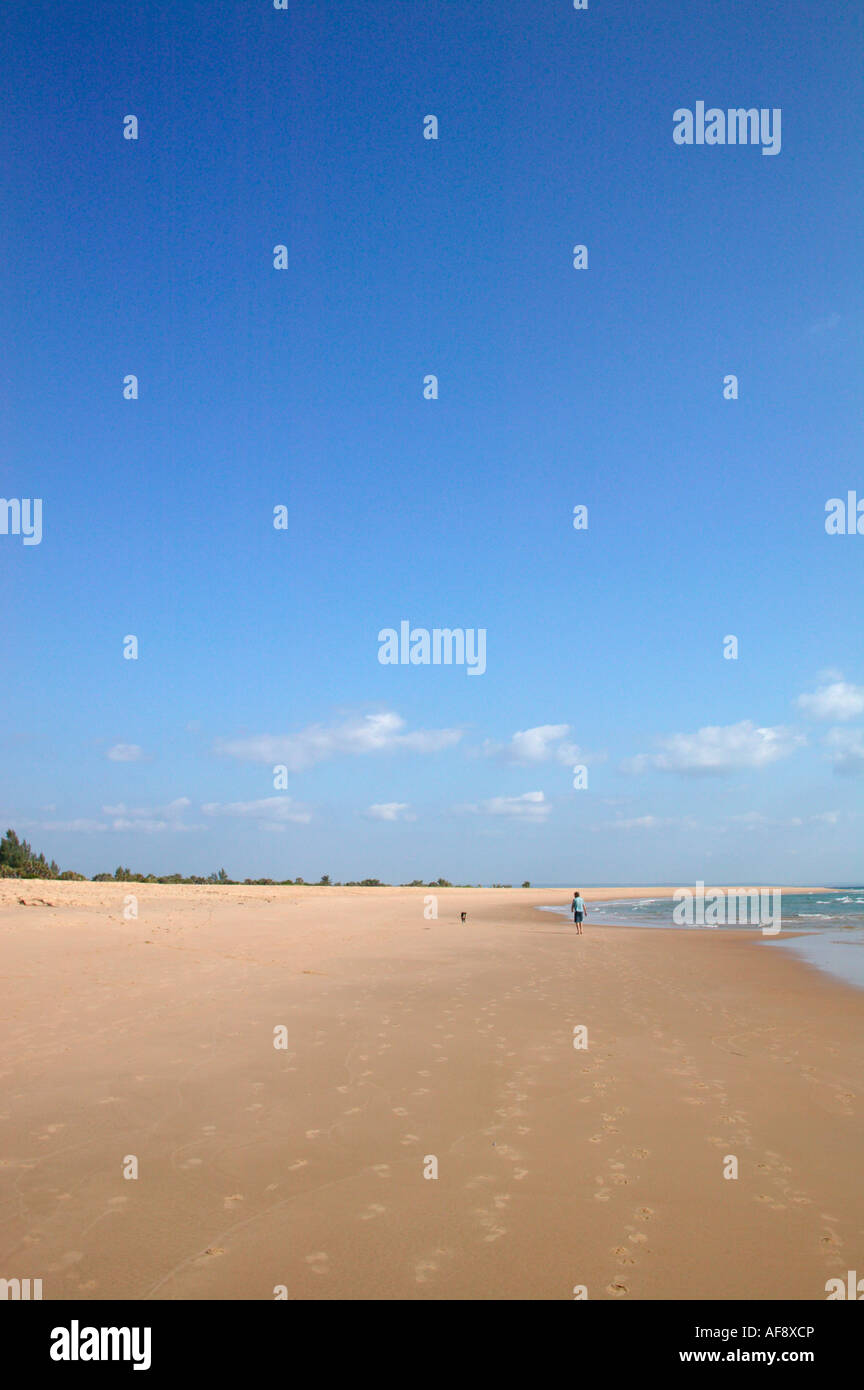 Footprints leading to a distant man walking on the beach with a dog Stock Photo