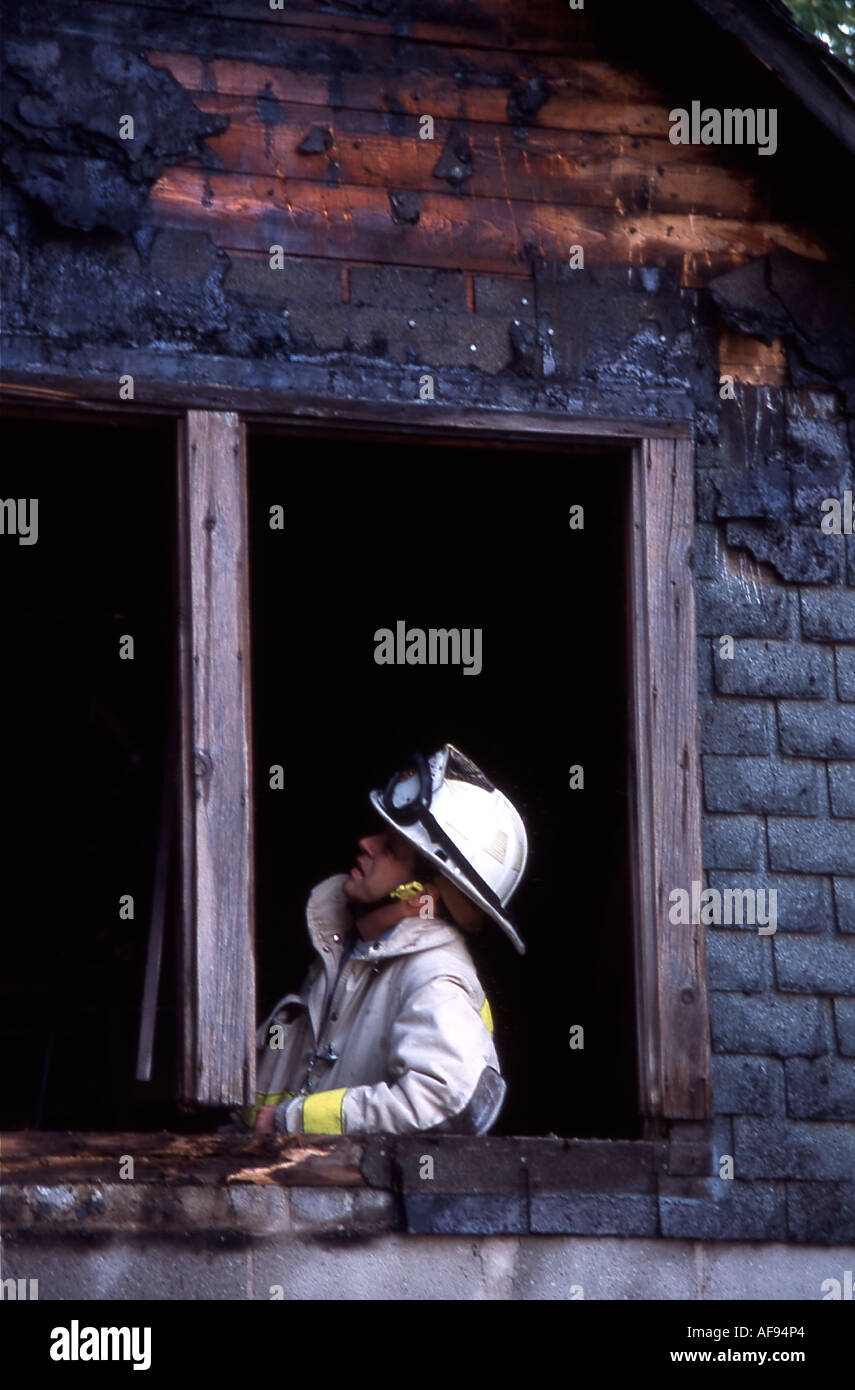A fire fighter investigating fire evidence in a burnt window frame of the burnt structure Stock Photo