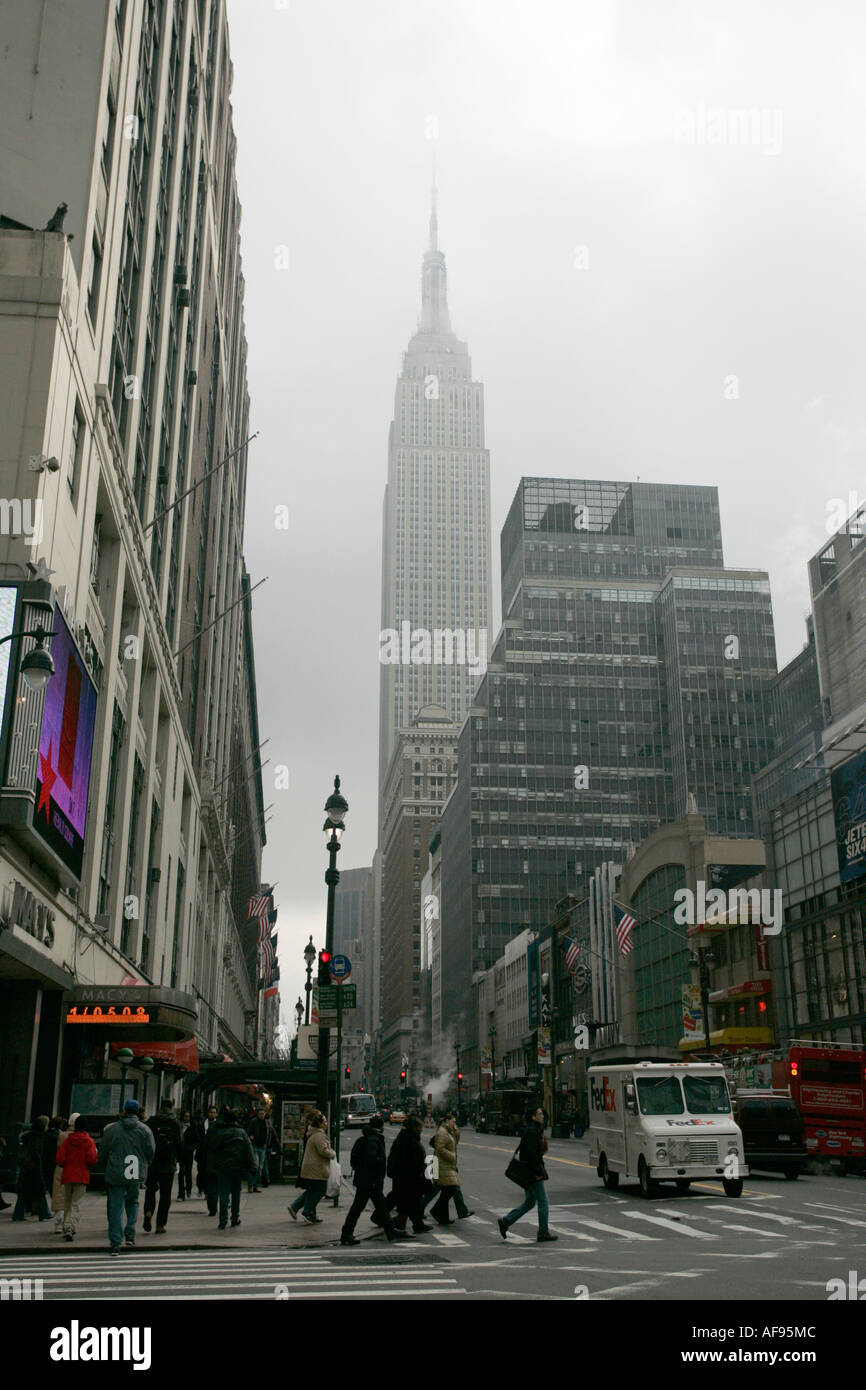 empire state building shrouded in mist as pedestrians crossing crosswalk on 7th ave and 34th street outside macys Stock Photo