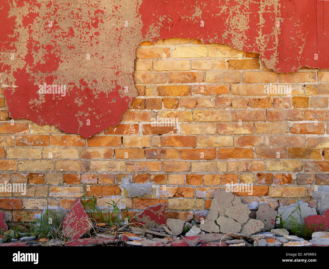 Painted red cement flaking off of an orange and yellow brick wall Stock