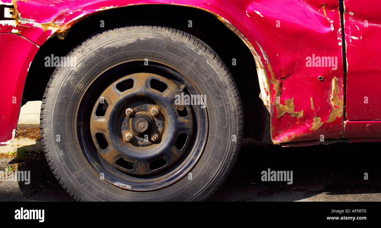 Damaged worn red or magenta car body and wheel showing dents corrosion dirt and other aging factors Stock Photo