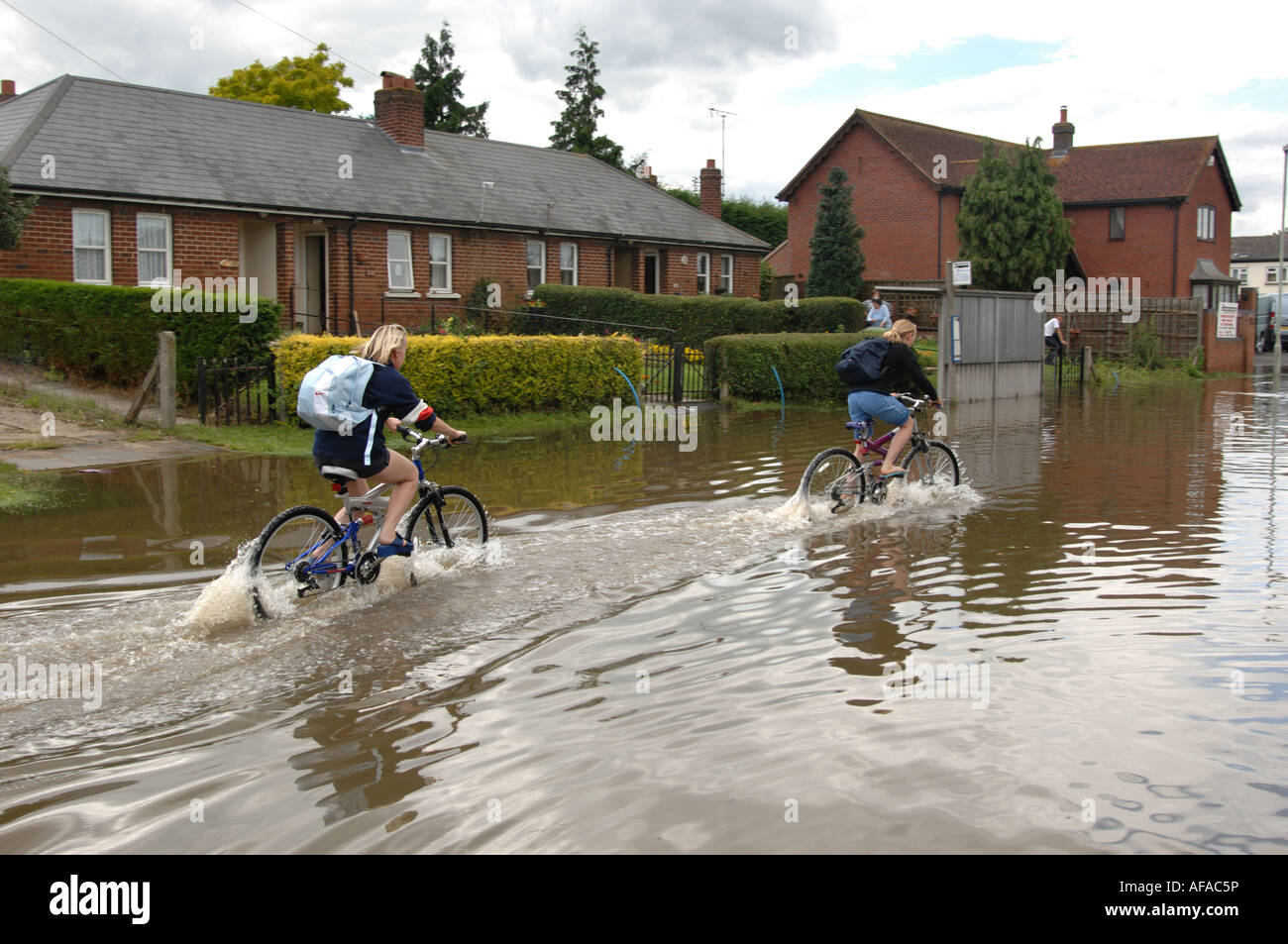 Two Women Cycling through the floods in the Longford area of Gloucester England July 2007 Stock Photo