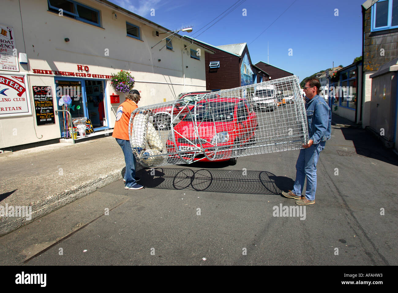 Richard Peirce, right, with Mally Toms carrying the cage to be used by divers to observe sharks off Looe in Cornwall, England Stock Photo