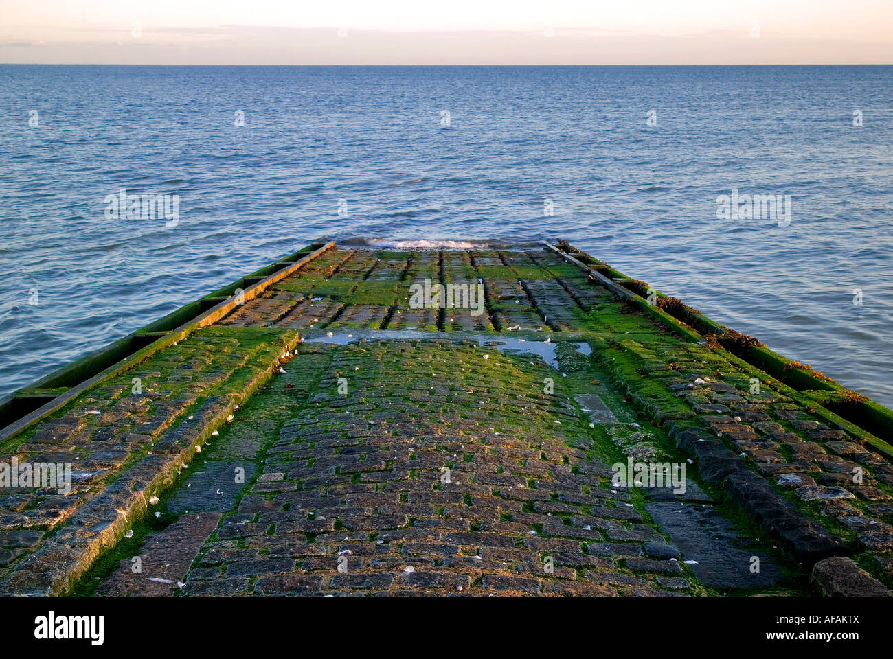 Cobbled boat slipway leading into the sea lit by the morning sun Stock Photo