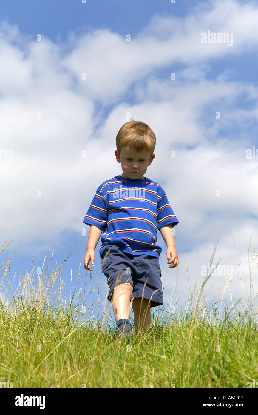 Little boy walking through a grass meadow on a bright summer s day Stock Photo